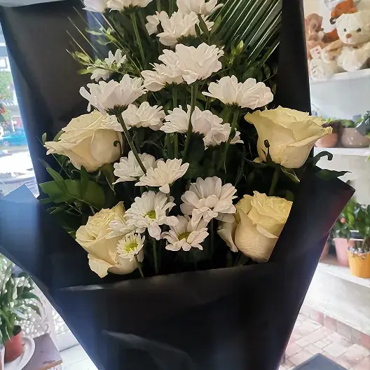 Buket belih krizantema i krem ruža u crnom papiru