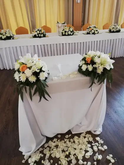 Dva aranžmana od belog i narandžastog cveća na stolu sa laticama